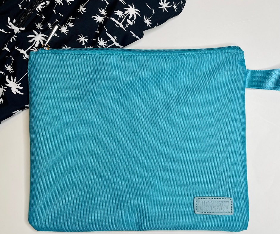 blue wet bag on a white background with palm print bikinis lying on top