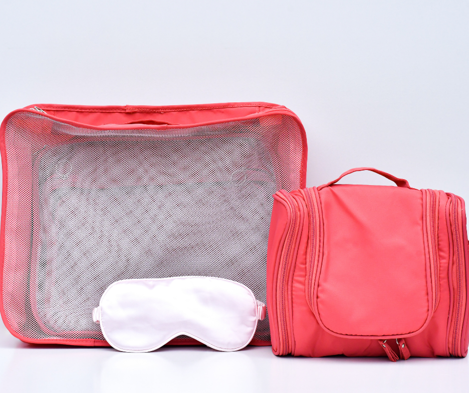 pink cosmetic case, packing cubes and sleep/eye mask on a white/light grey background