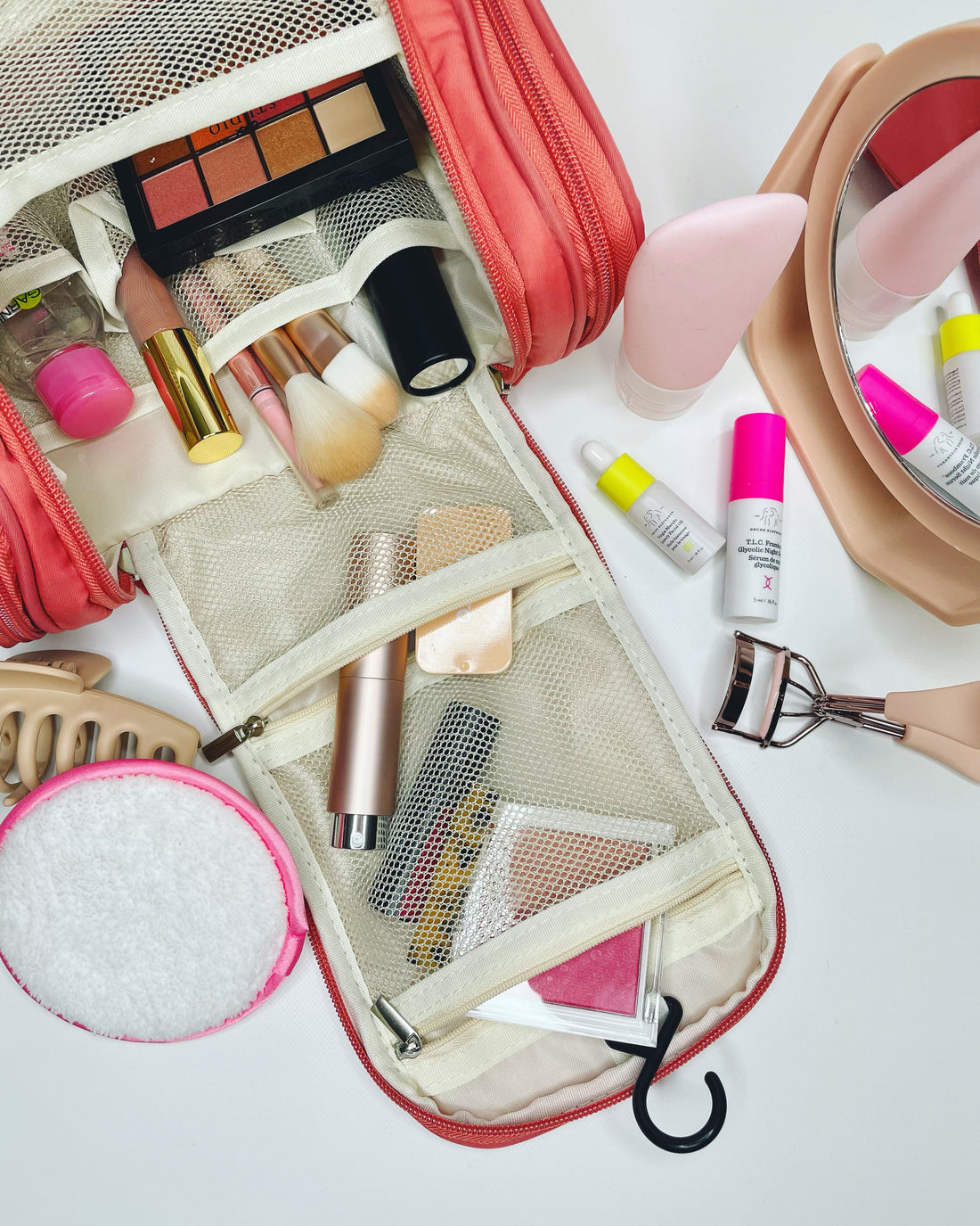 pink cosmetic case on a white background with cosmetics displayed around it 