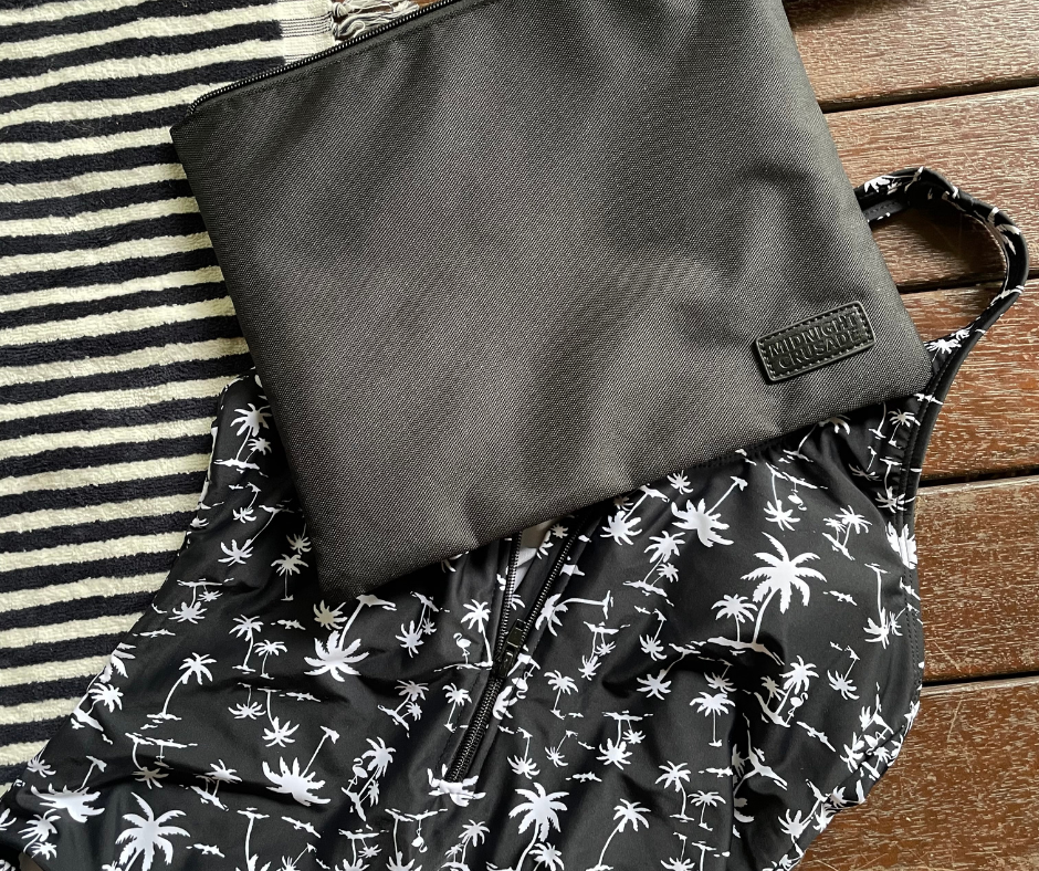 black wet bag on a beach towel and palm print black swimmers