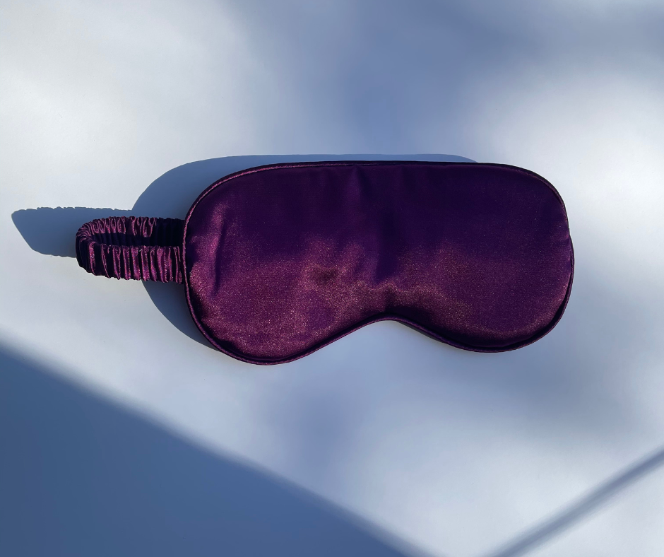 deep purple sleep/eye mask on a white background with sun shining on it 