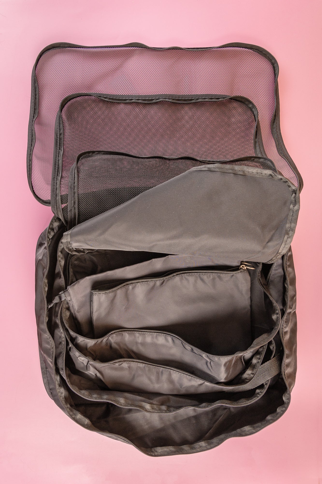 black packing cubes opened up on a pink background