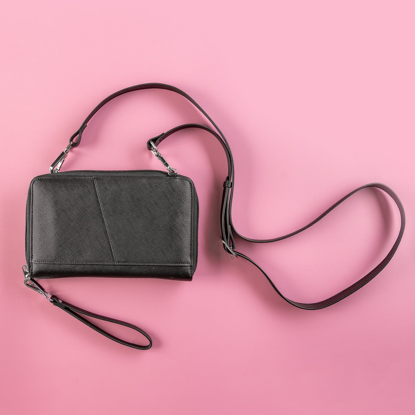 black passport wallet with wrist and bag strap on a pink background