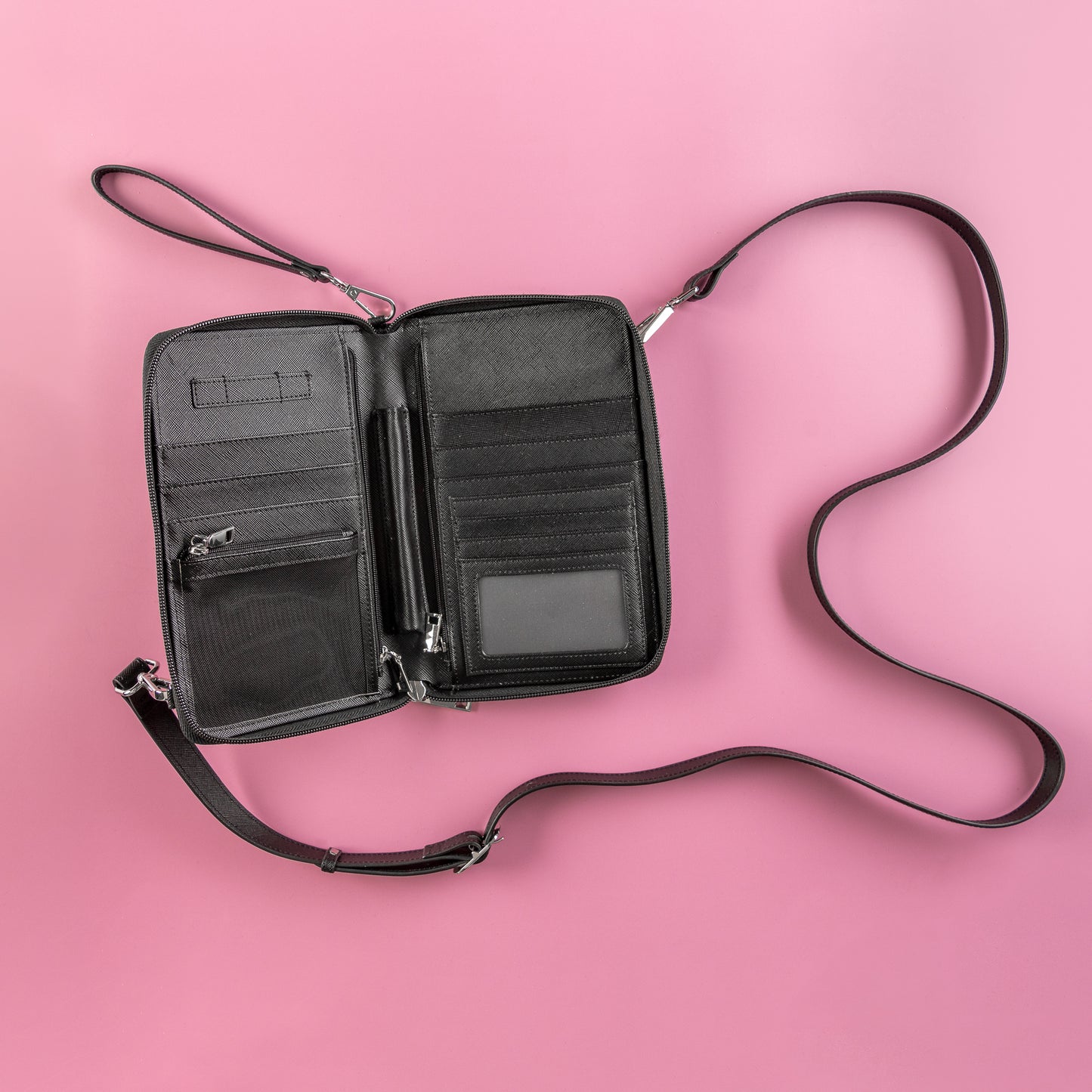 black passport wallet with wrist and bag strap on a pink background showing plenty of room for pen, sim cards, passports, boarding passes, cash & cards