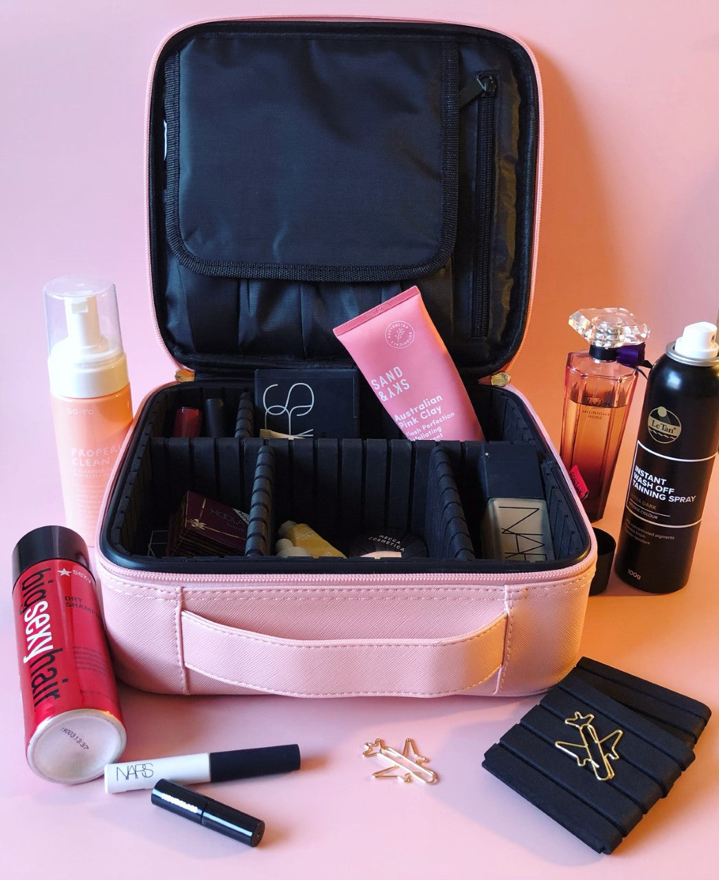 pink cosmetic case on a pink background with cosmetic products lying around it 