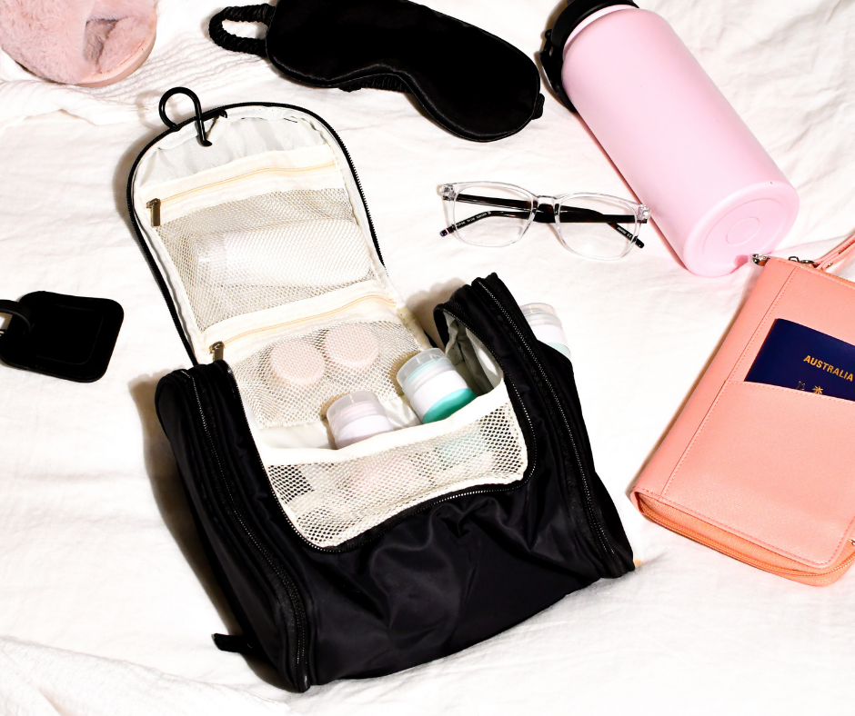 black hanging cosmetic case on a white bed with a few travel essentials laid out next to it
