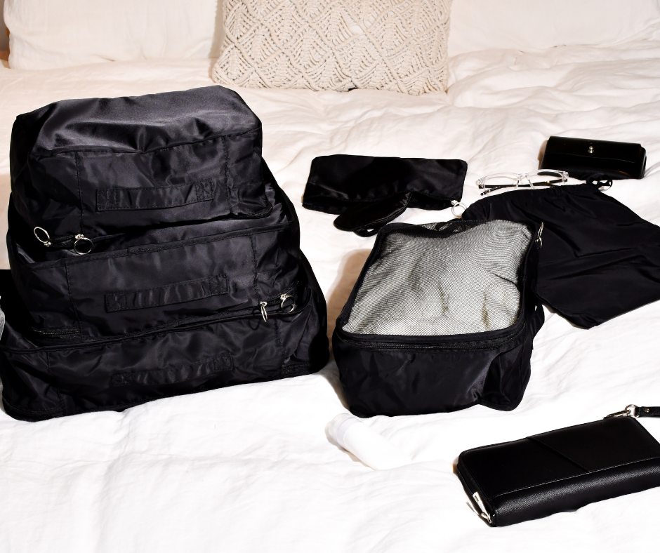 black packing cubes and passport wallet on a white bed cover all laid out and ready to be packed for a holiday