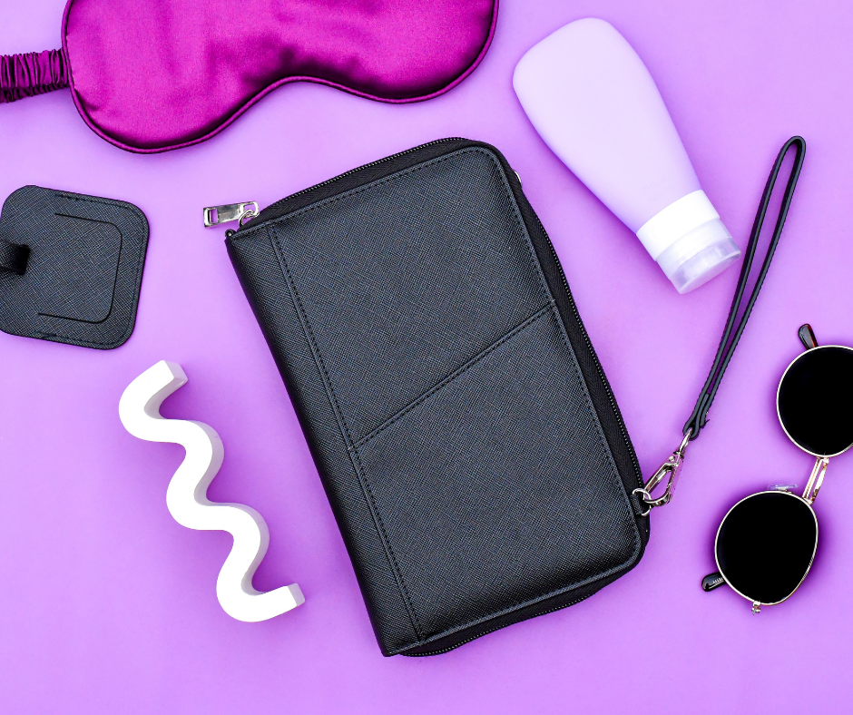 black travel bag on a purple background with purple sleep mask, travel bottle, luggage tag and sunglasses also laid out