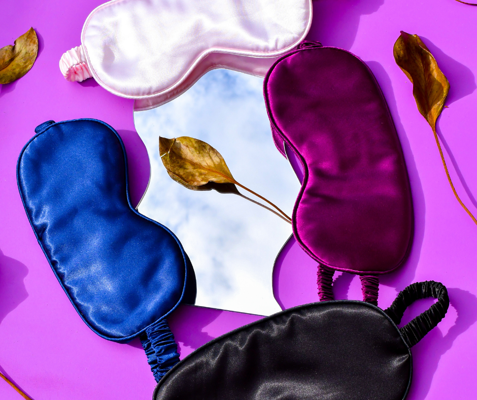 4 colourful sleep/eye masks laid out on a purple background with leaves and a mirror spread out around them