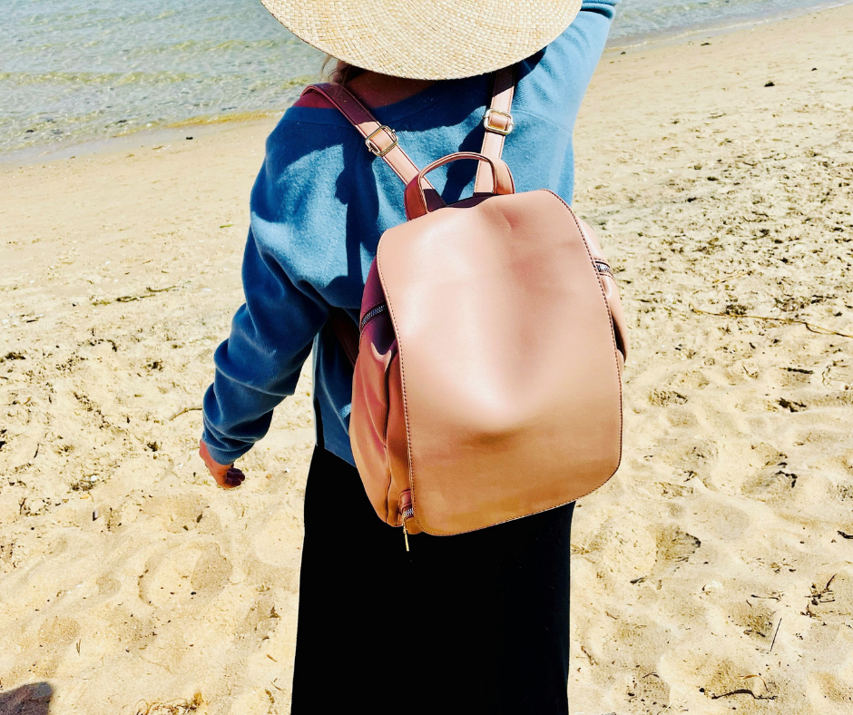 woman in a blue sweater and black skirt on a beach with the tan backpack from midnight crusade on.