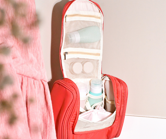 pink hanging cosmetic case shown packed with travel bottles and hanging up in a bathroom