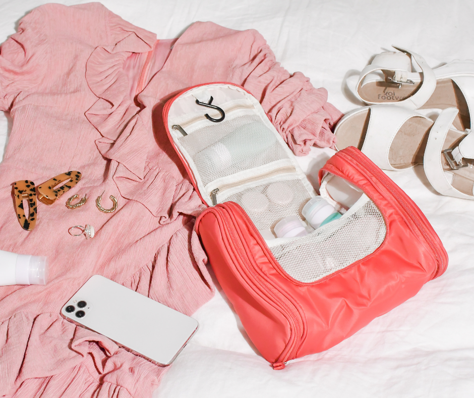 pink hanging cosmetic case on a bed with clothes and travel accessories spread out next to it. ready for a holiday!