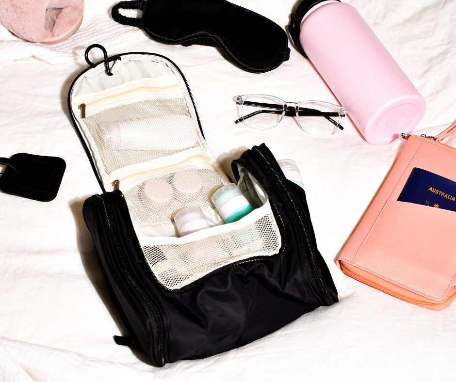 black hanging cosmetic case on a bed with travel accessories laid out next to it - ready for a holiday!