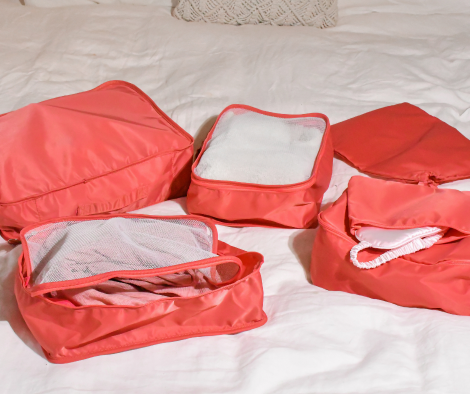 pink packing cubes spread out on a bed with other travel accessories. ready to be packed for a holiday!